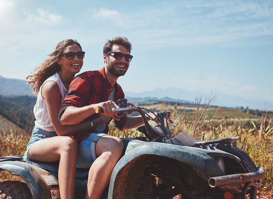 Off-Road Vehicle Insurance - Happy Young Couple Riding ATV Together Along a Dirt Road in the Countryside on a Sunny Day