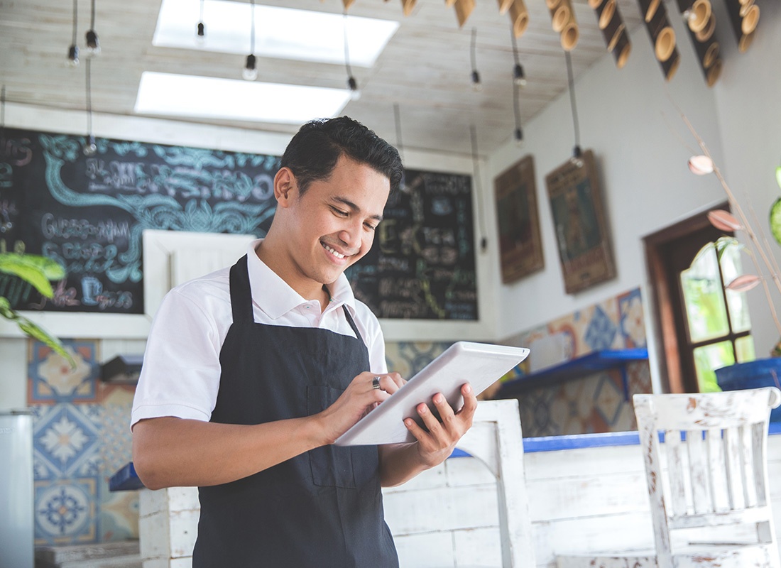 Business Insurance - Portrait of a Smiling Young Small Business Owner Standing in his Cafe While Holding a Tablet in his Hands