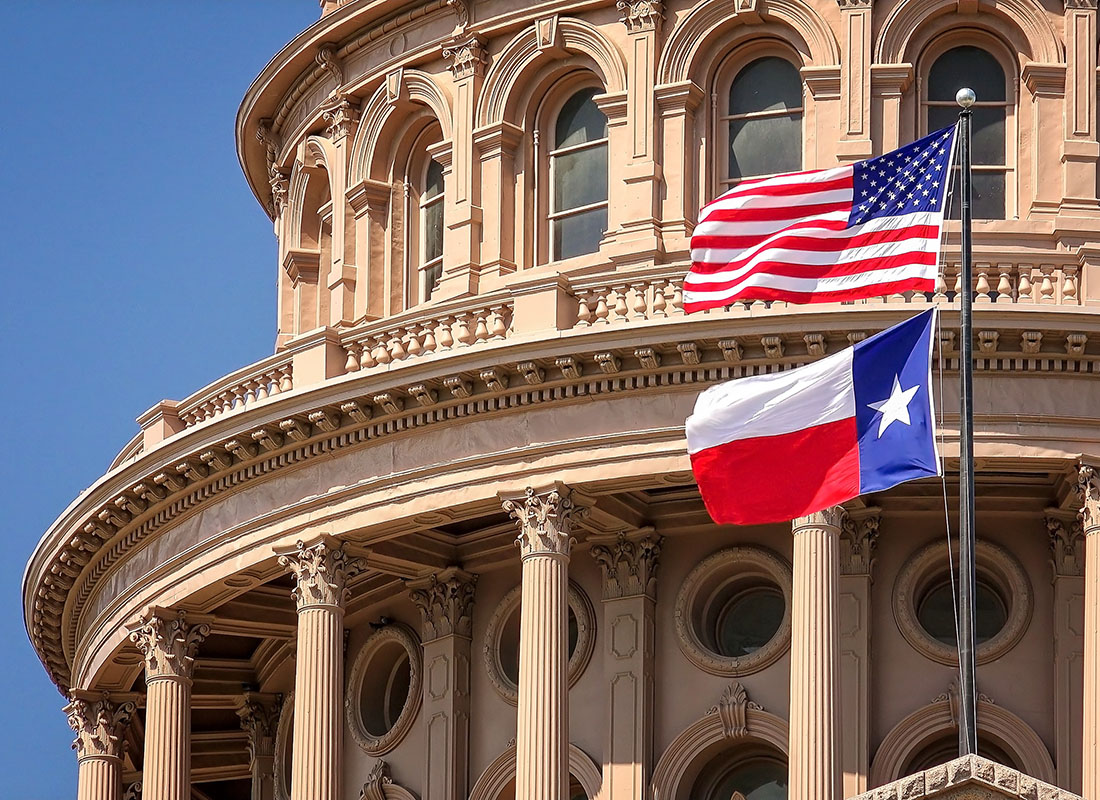 Our Organizations - Closeup View of the State Capitol Building of Texas Against a Bright Blue Sky with the American and Lone Star Flag in Front