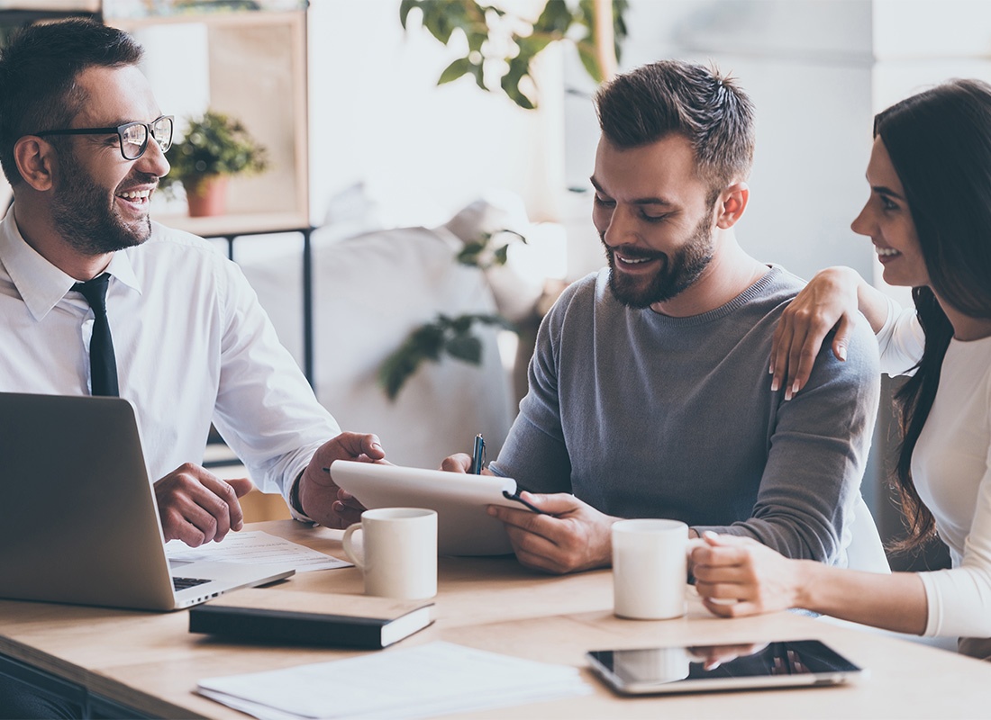 Insurance Consulting Services - Cheerful Young Insuranced Agent Sitting in a Meeting with a Young Married Couple in the Office Helping Them with Paperwork